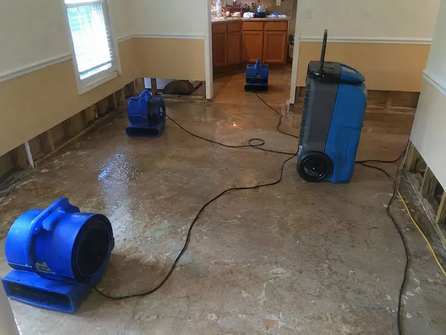 Air movers and a dehumidifier drying a flooded room after the baseboards were removed