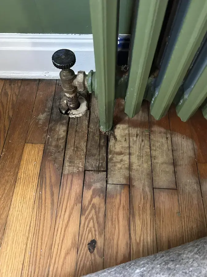 Old cast iron radiator valve with water damaged hardwood floor below